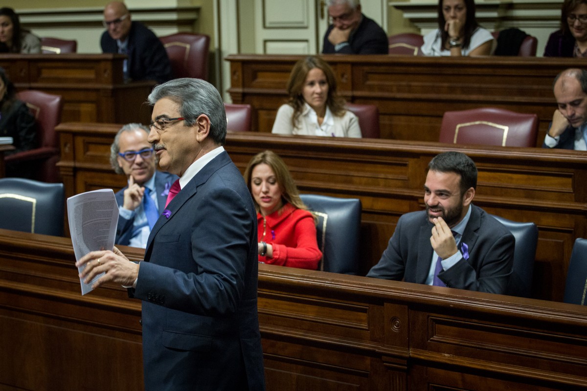Román Rodríguez (de pie) y Aarón Afonso (sentado, primero por la dcha.), durante un pleno del Parlamento canario. / ANDRÉS GUTIÉRREZ