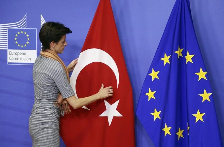 Una mujer ajusta la bandera de Turquía próxima a la de la Unión Europea antes de la llegada del primer ministro turco, Davutoglu, a la reunión de líderes de la UE, en Bruselas | FOTO: REUTERS/Francois Lenoir