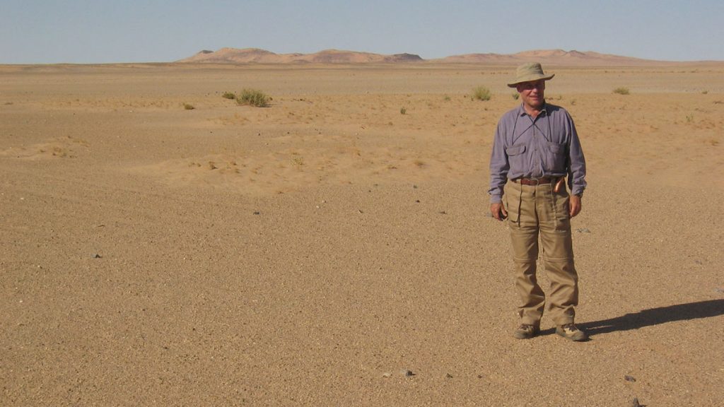 Francisco García-Talavera, en el desierto mauritano en una de las expediciones; al fondo se aprecia el cráter Tenoumer, cuya magnitud se capta en la imagen superior en una foto de la NASA desde el espacio. DA