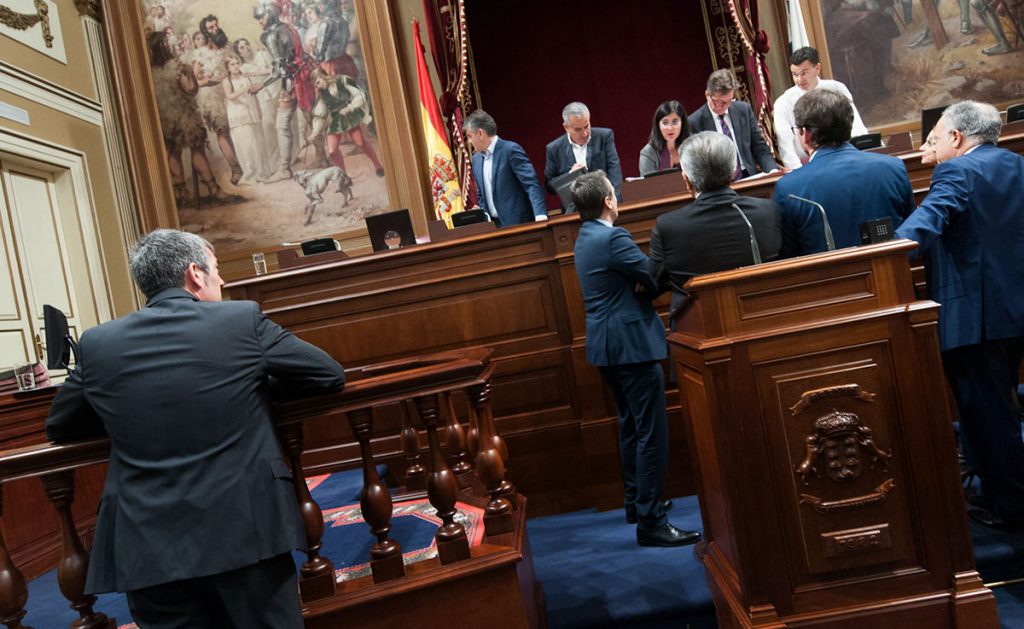 Fernando Clavijo, de espaldas en primer plano, observa a los portavoces de la oposición debatiendo un asunto con los miembros de la Mesa del Parlamento. Andrés Gutiérrez