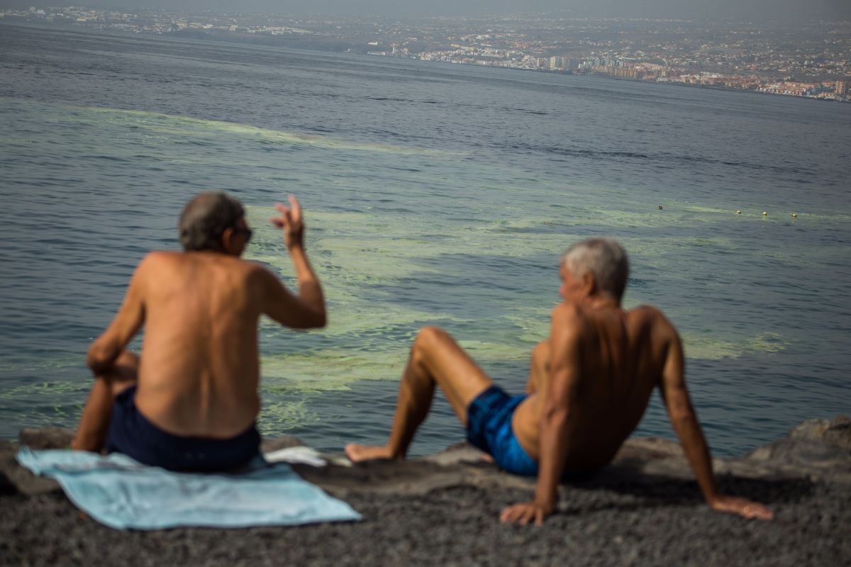 Unos bañistas, ayer, sentados en Radazul, con las manchas de cianobacterias frente a ellos. Andrés Gutiérrez