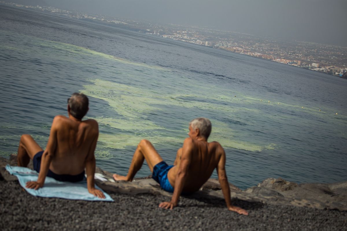 Unos bañistas, ayer, sentados en Radazul, con las manchas de cianobacterias frente a ellos. Andrés Gutiérrez