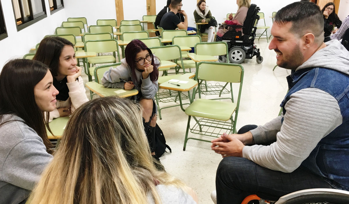 Varias alumnas conversan con un voluntario con discapacidad en un aula. DA