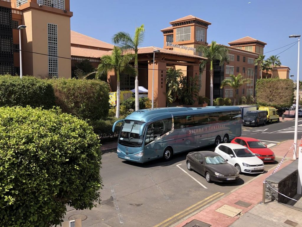 A la izquierda, momento en el que la tercera guagua con turistas británicos sale del hotel H10 Costa Adeje Palace en dirección al Aeropuerto Tenerife Sur. Arriba, varios evacuados en el interior del vehículo, huéspedes en los balcones y uno de los precintos de seguridad. J.C.M.
