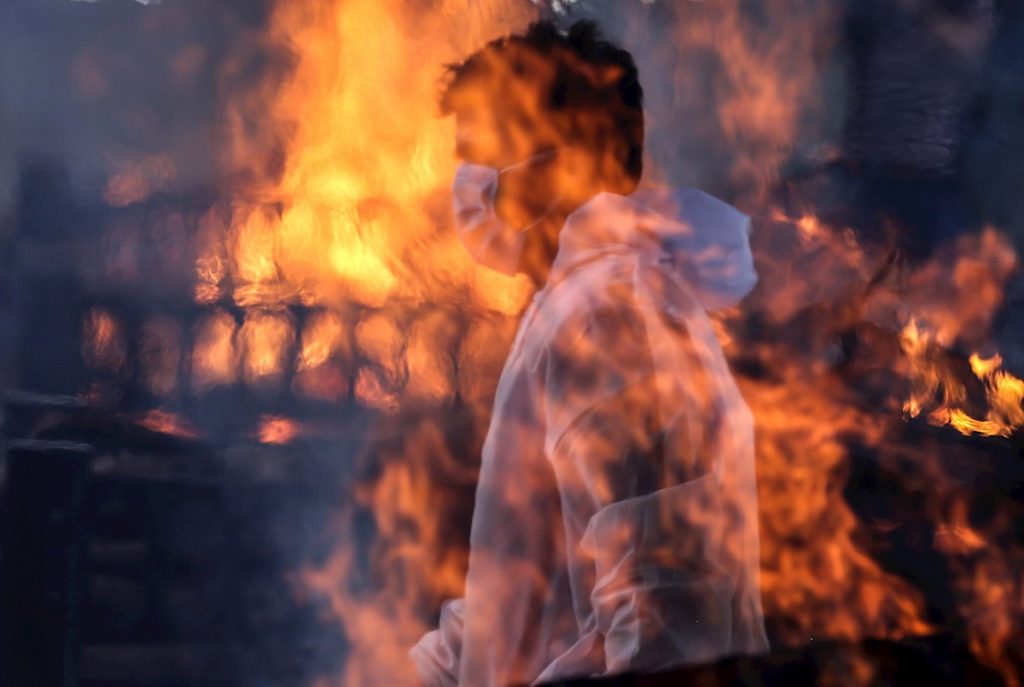 Un trabajador municipal con EPI visto tras las llamas de una de las hogueras prendidas en un crematorio para víctimas de la covid-19, este viernes en Bombay, India. EFE/ Divyakant Solanki