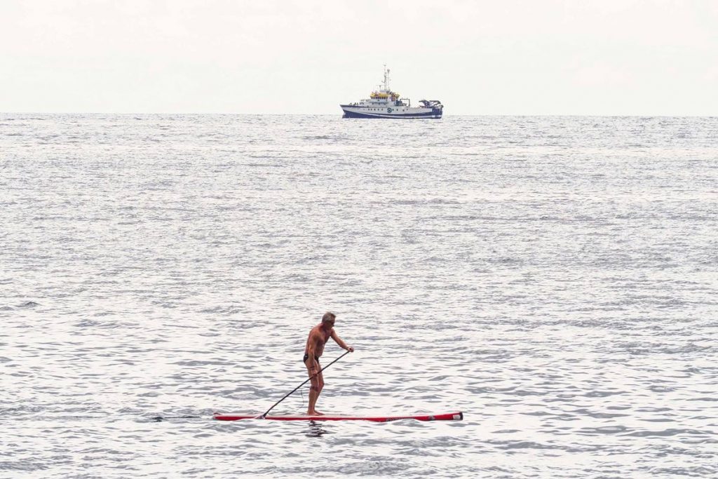 Un deportista practica con el buque oceanográfico en plena faena como telón de fondo. Sergio Méndez