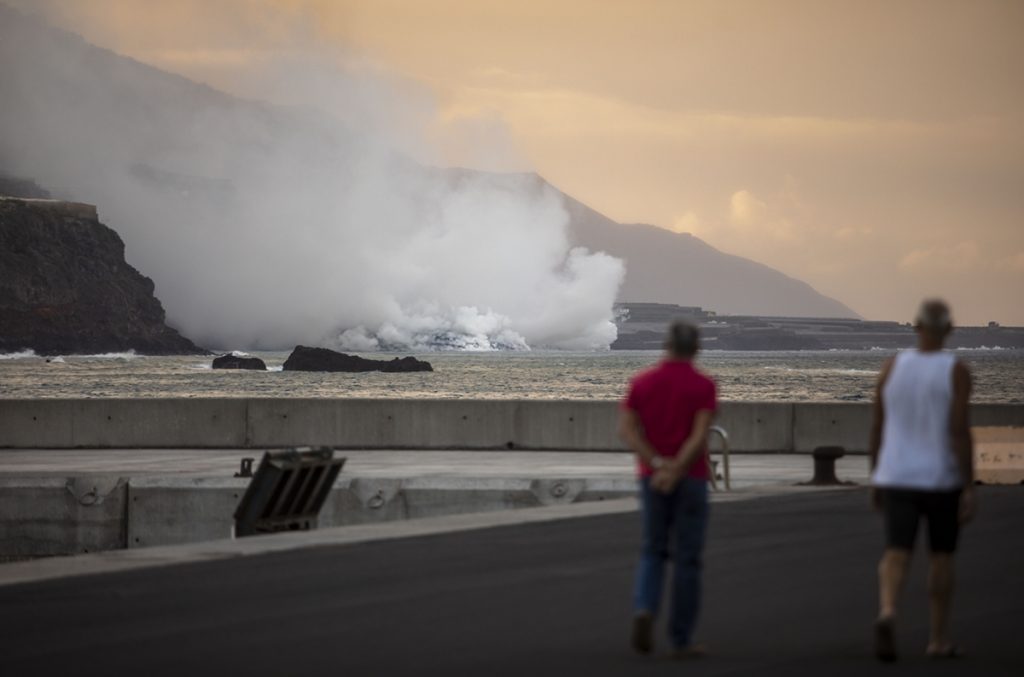 Dos personas observan la columna de humo y la lava del volcán de Cumbre Vieja a su llegada al Océano Atlántico. | EP