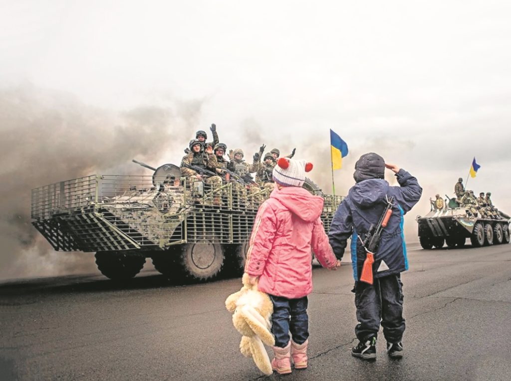 Dos niños saludan a los tanques del Ejército de Ucrania cuando se dirigían ayer a defender la capital, Kiev, del ataque masivo de las tropas rusas. DA