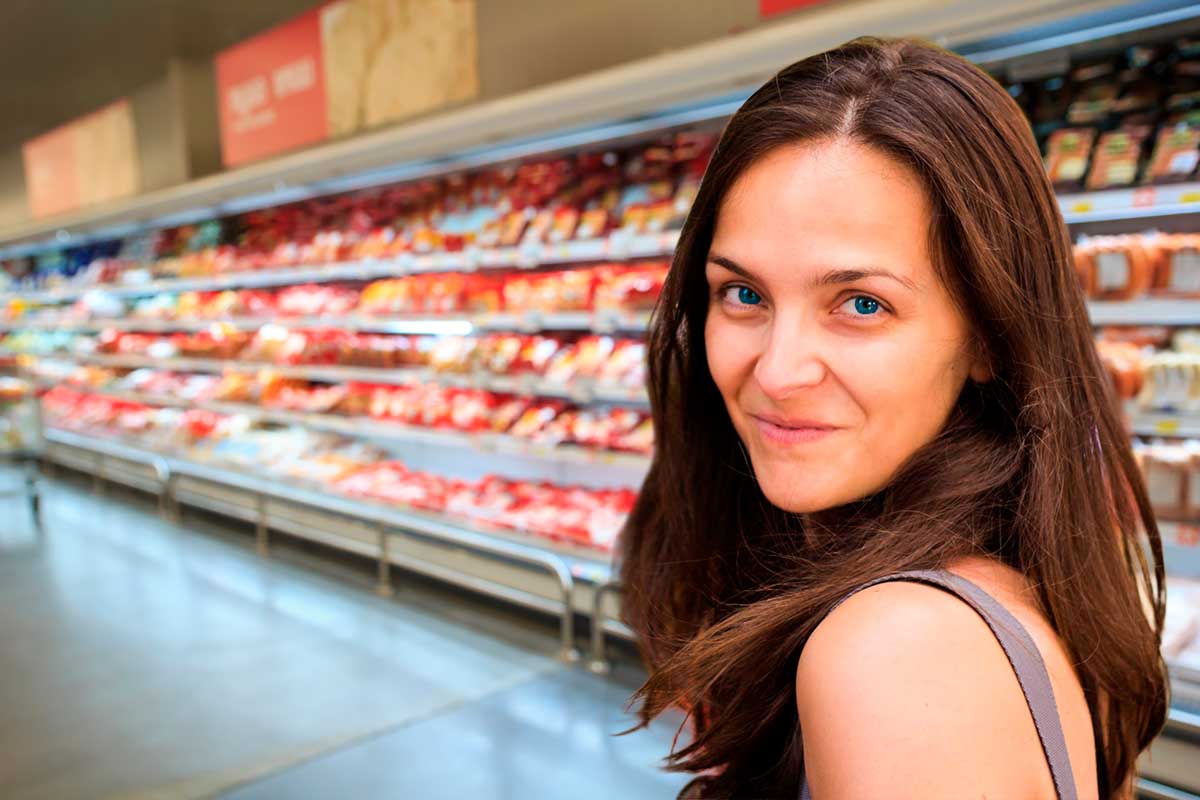 María Alcázar mirando al lector mientras recorre un pasillo de embutidos en un supermercado