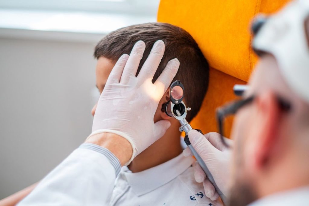 Un otorrinolaringólogo realiza una otoscopia a un niño utilizando un otoscopio profesional, mientras lleva guantes médicos, en una consulta de salud auditiva