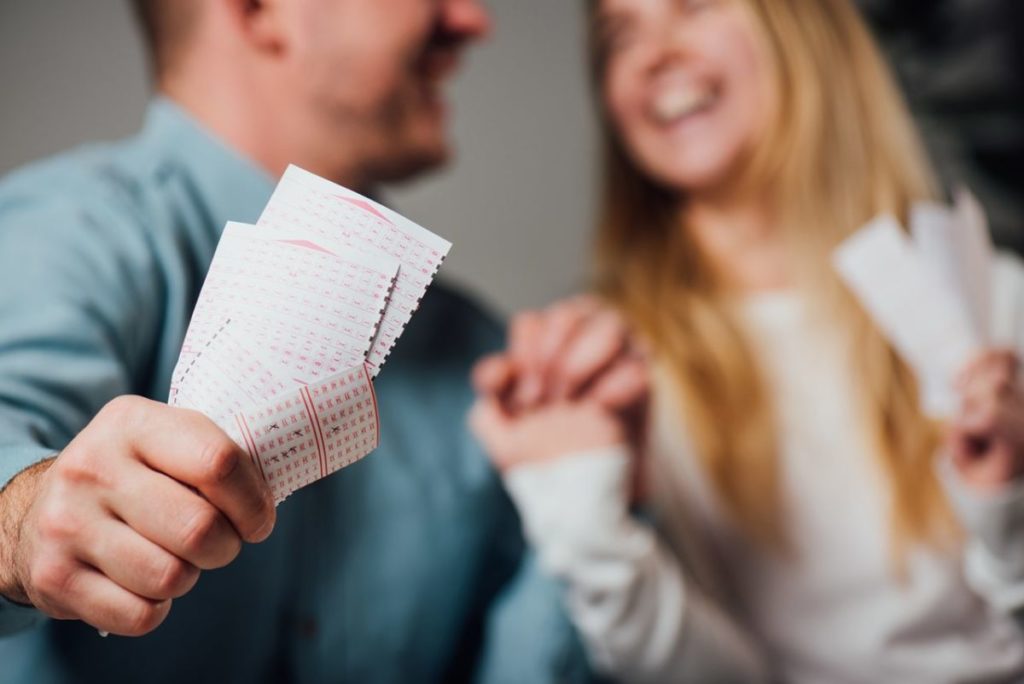 Una pareja sonriente sostiene varios boletos de lotería, en una imagen de recurso que ilustra la felicidad tras ganar un premio en un sorteo de apuestas