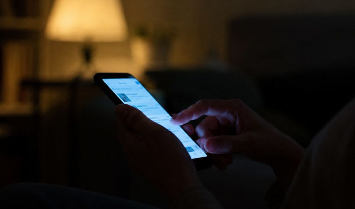 Trabajadora en la cama de noche leyendo un mensaje de WhatsApp de su jefe que vulnera el derecho a las multas por desconexión digital