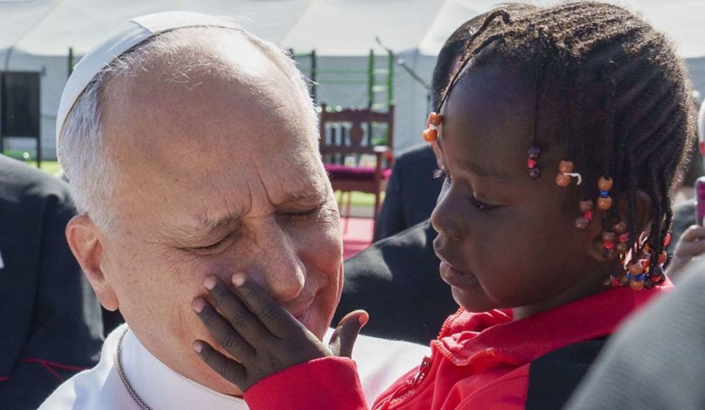 El papa León XIV coge en brazos a una niña migrante en Las Raíces, en La Laguna. | Ramón de la Rocha / Efe