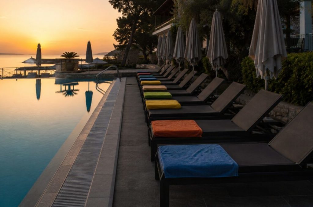 Fila de hamacas vacías con toallas de colores para reservar sitio junto a la piscina de un hotel al amanecer