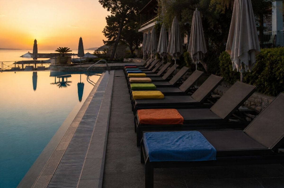 Fila de hamacas vacías con toallas de colores para reservar sitio junto a la piscina de un hotel al amanecer