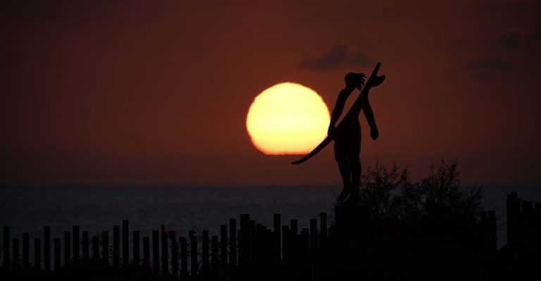 El sol se pone sobre el mar mientras la silueta de una persona con una tabla de surf recorta el horizonte en Punta Blanca, en Guía de Isora. | Eduardo García