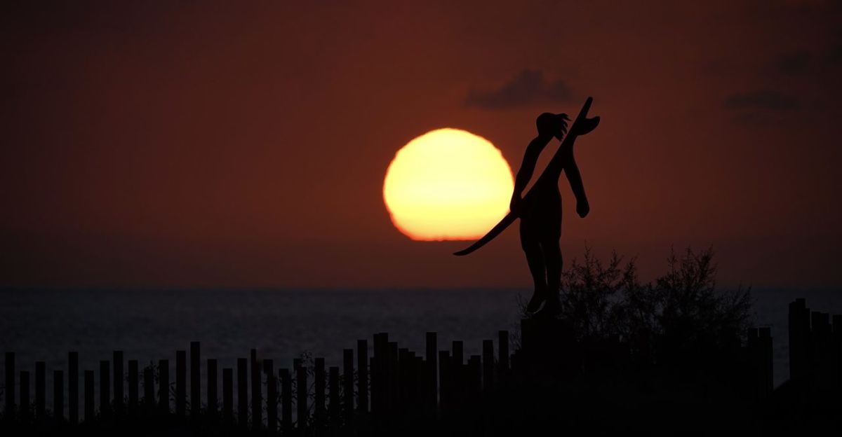 El sol se pone sobre el mar mientras la silueta de una persona con una tabla de surf recorta el horizonte en Punta Blanca, en Guía de Isora. | Eduardo García