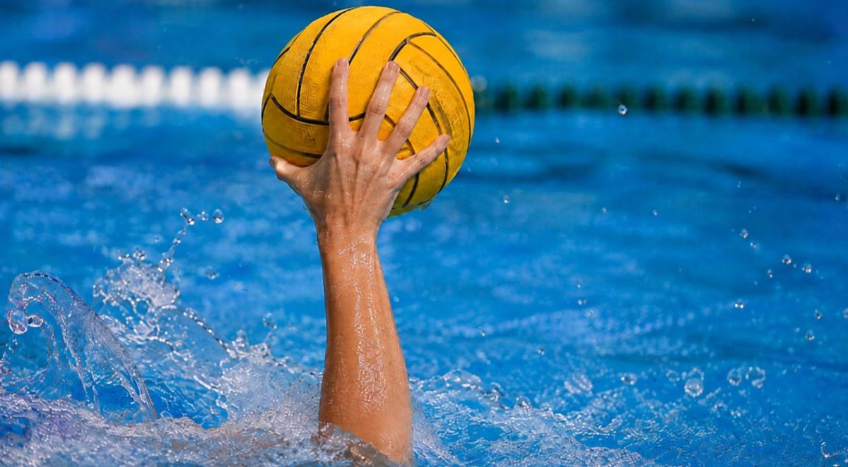 Una jugadora de waterpolo sostiene el balón sobre el agua durante una acción de juego en la piscina.