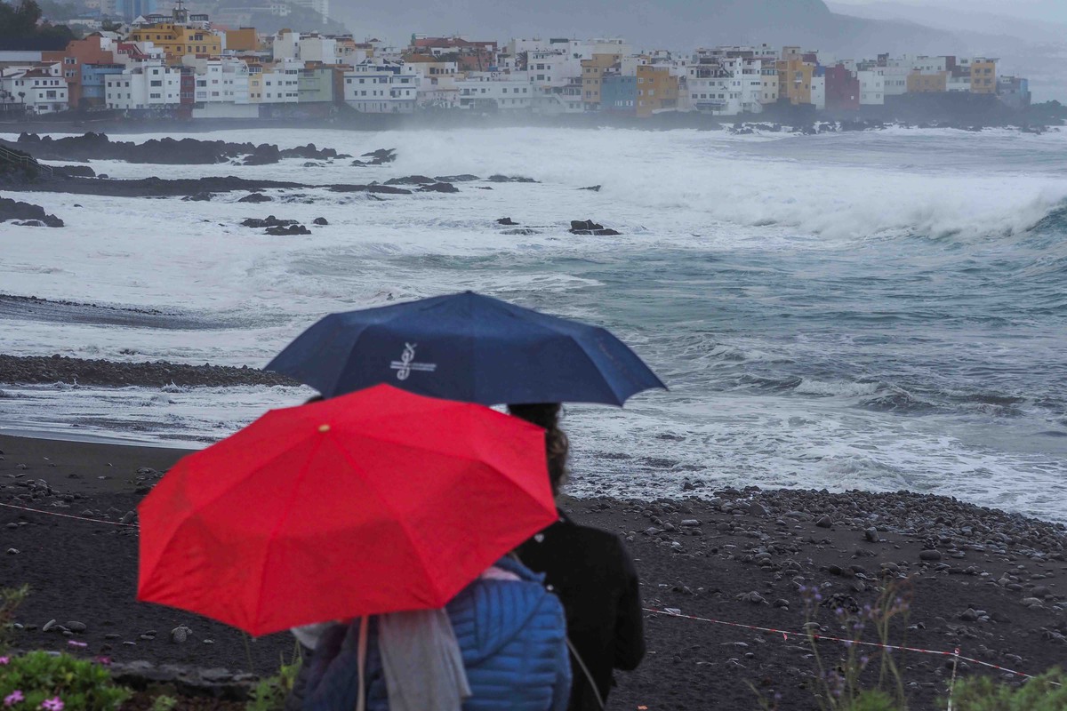 Personas con paraguas junto a la costa del norte de Tenerife, con fuerte oleaje y cielo cubierto